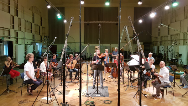 Musiker:innen sitzen mit ihren Instrumenten. Um sie herum sind viele Mikrofone.