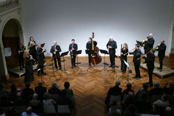 Musiker:innen stehen auf einer Bühne in einer Reihe. Im Vordergrund das Publikum.