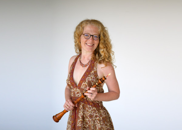 Fotografie einer Frau mit einem Instrumente in der Hand, die in die Kamera lächelt